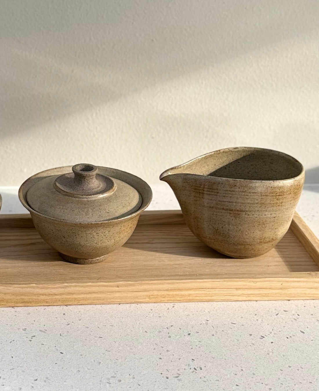 Gaiwan med lokk og en liten keramikkkanne på et trebrett i varmt sollys.
